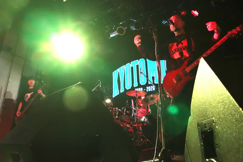KYOTO MUSE でのライブ。緑の照明が差し込むステージで赤いギターを弾くメンバー